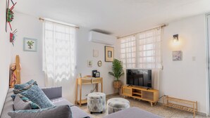 Ein Wohnzimmer mit einer Couch, Hocker, einem Fernseher und einem Holztisch.