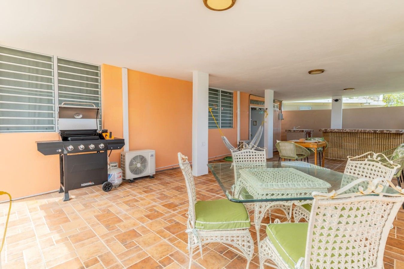 Une terrasse extérieure avec un barbecue, des meubles en osier et un ventilateur.