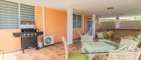 Une terrasse extérieure avec un barbecue, des meubles en osier et un ventilateur.
