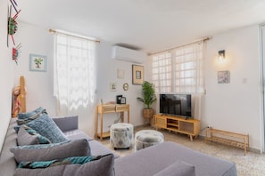 Ein Wohnzimmer mit Sofa, Hocker, TV-Schrank und einer Pflanze.