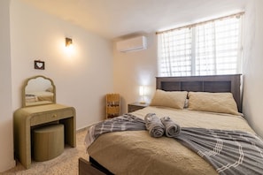 Ein Schlafzimmer mit einem Bett, einem Nachttisch, einem Spiegel, einer Lampe und einer Klimaanlage.