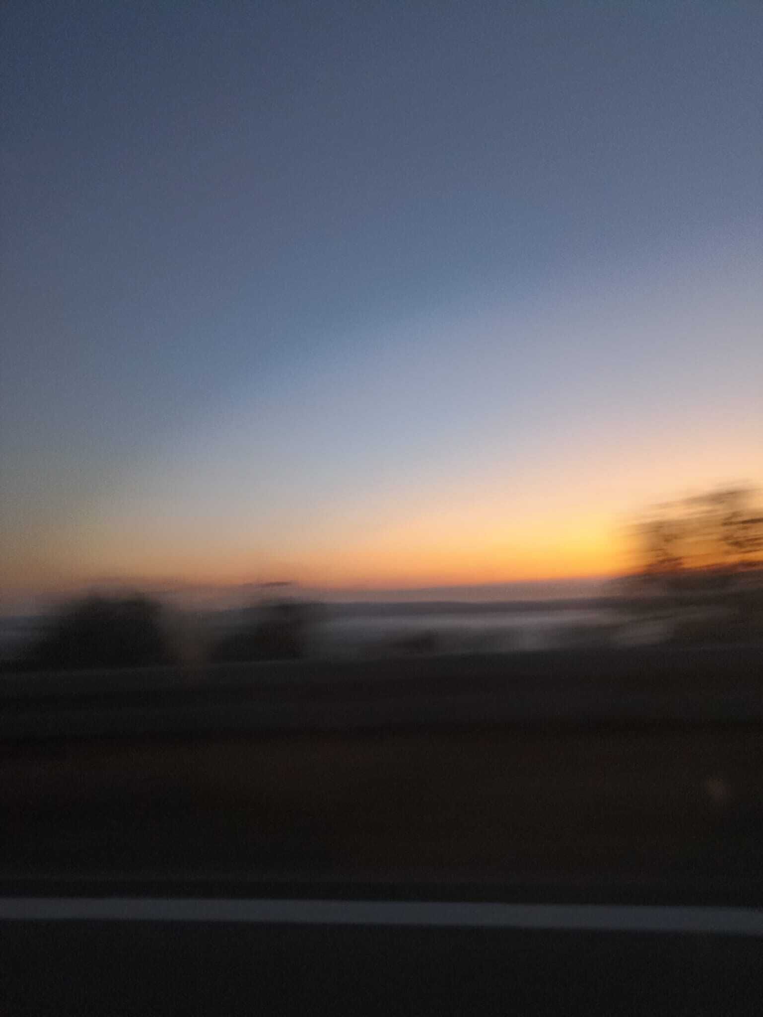 A blurred view of a sunset over a flat landscape with a road in the foreground.
