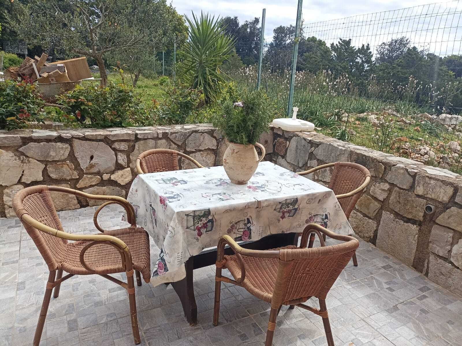 En uteplats med en mur av sten, flätade stolar, ett bord med ett blommigt tyg och en krukväxt.