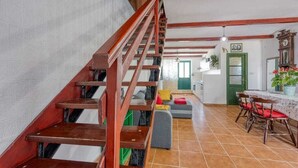 A staircase with wooden railings, a dining area with a table and chairs, and a green door in the background.