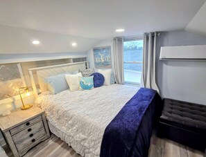 Ein Schlafzimmer mit Bett, Nachttisch, Lampe und einem Fenster mit Vorhängen.