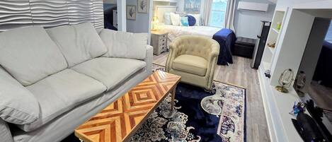 A modern hotel room with a sofa, armchair, patterned rug, and a bed with a view.