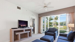 A modern living room with a flat-screen TV, a ceiling fan, and a large window offering a view of palm trees. - #411 - First Floor, Sleeps 6 - Landscape View (Naples)