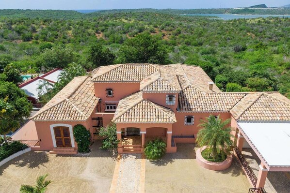 A large, single-story building with a tiled roof, surrounded by lush greenery and a clear view of the landscape. - Hacienda Célèbre, Curaçao (Jan Thiel)