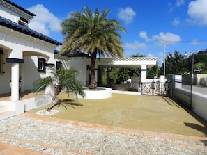 A white building with a tiled patio, palm trees, and a covered outdoor seating area. - Hacienda Célèbre, Curaçao (Jan Thiel)