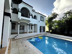 Uma casa de dois andares com piscina, área de estar externa e um jardim.