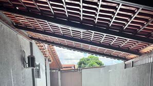 A covered outdoor area with a tiled floor, metal railings, and a view of a residential building in the background. - House (two-story house) for 9 people, very close to MotoGP. (Goiânia)