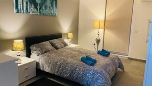 Hotellihuone, jossa on sänky, kaksi yöpöytävalaisinta, taulu seinällä ja ovi.