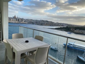 Ein Balkon mit Korbmöbeln, der auf einen Hafen mit Booten und historischen Gebäuden blickt.