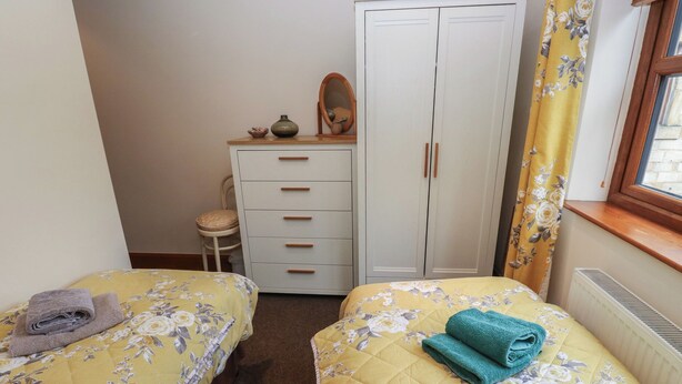 A bedroom with two beds, a wardrobe, a chair, and a window with curtains. - Green Route Apartment (Todmorden)