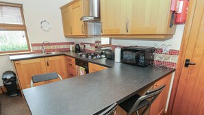 A kitchen with wooden cabinets, a gas stove, a microwave, and a sink. - Green Route Apartment (Todmorden)