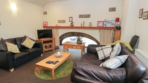 A living room with a sofa, a coffee table, a TV, and a fireplace. - Green Route Apartment (Todmorden)
