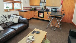 A compact kitchen with wooden cabinets, a stainless steel range hood, and a dining area with a foldable table. - Green Route Apartment (Todmorden)