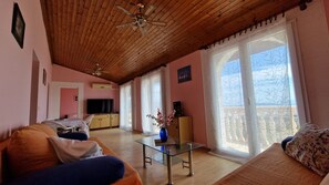 Ein Wohnzimmer mit Holzbalkendecke, einem Glastisch, einer Couch und einem Fernseher.