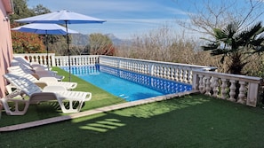 Ein Swimmingpool mit weißer Brüstung, umgeben von Kunstgrün und weißen Liegestühlen.