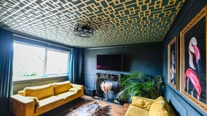 A room with a patterned ceiling, a sofa, a fireplace, a television, and a painting. - Bold boudoir interiors, private patio and steps from the beach (West Sussex)