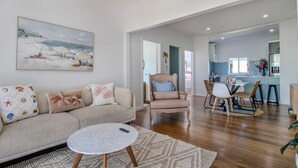 Un salon avec un canapé, une table basse ronde et un tableau représentant une scène de plage.