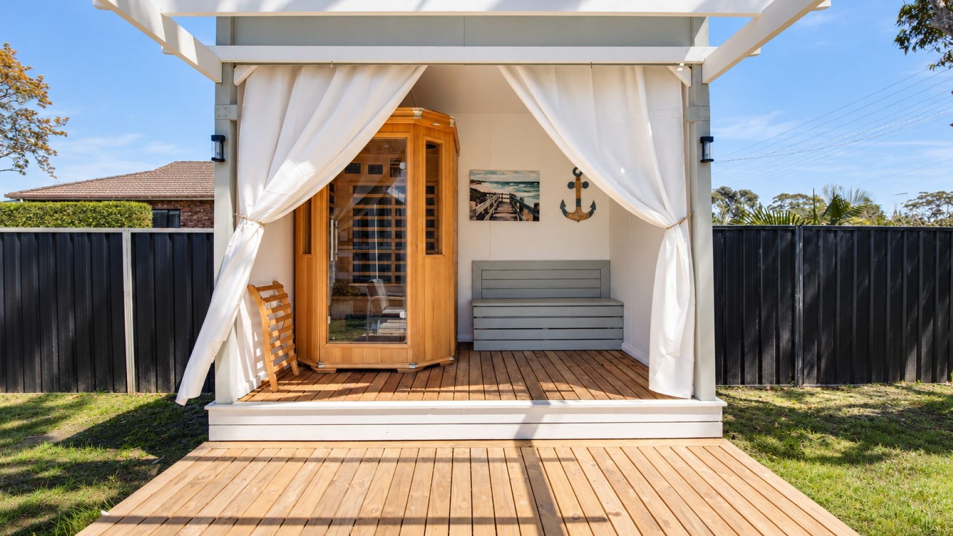Una terraza de madera con un espacio de estar cubierto, una sauna de madera y un banco.