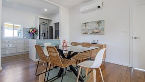 Une cuisine moderne avec un coin repas, comprenant une table en verre, des chaises en osier et un tableau au mur.