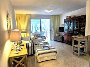 Una sala de estar con sofá, sillón, reposapiés, lámpara y un mueble con botellas.