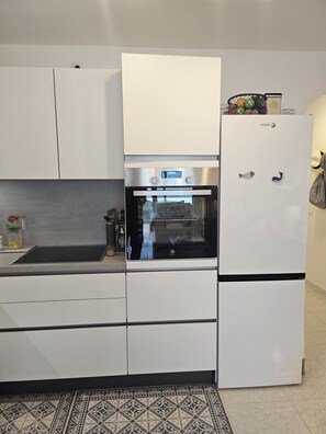 Una cocina moderna con armarios blancos, horno empotrado y refrigerador.