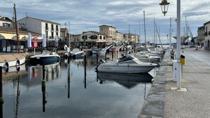 Un puerto deportivo con barcos amarrados a lo largo de la costa, edificios con señalización y un paseo peatonal.