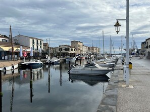 A marina with boats docked along a waterfront, buildings with signage, and a pedestrian walkway. - Summer in Marseillan – the pearl of Languedoc. (Marseillan)