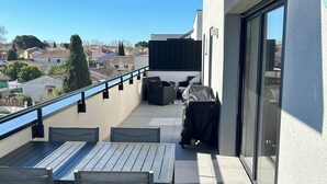 Un balcón con mesa y sillas, una parrilla cubierta y vistas de la ciudad.
