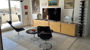 Una sala moderna con un televisor de pantalla plana grande, dos sillas negras, un mueble de madera y una escultura decorativa de jirafa.