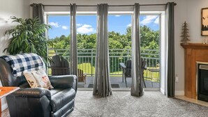 Une pièce avec un canapé en cuir noir, une cheminée et un balcon donnant sur un paysage verdoyant.