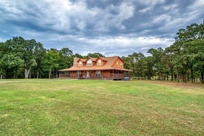 A large two-story house with a porch, surrounded by a grassy yard and trees.