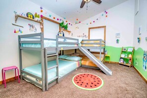 A bunk bed room with a slide, a small stool, and a watermelon rug.