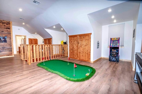An indoor mini-golf setup with a wooden fence, a green putting surface, and a pinata machine.