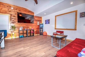 A room with a wooden accent wall, a TV, a gaming console, and a red sofa.