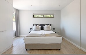 Un dormitorio moderno con una cama grande, mesitas de noche, una ventana con cortinas y una lámpara en el techo.