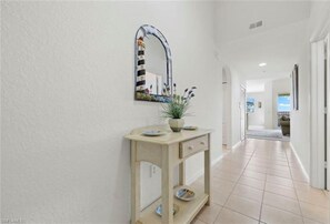 A hallway with a light-colored console table, a mirror with a decorative frame, and a potted plant. - Stunning 2 BR/2 BA Naples Golf Resort condo - 4 miles to 5th Ave shops & beaches (Naples)