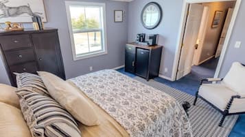 A bedroom with a bed, a dresser, a desk with a coffee maker, a chair, and a window.