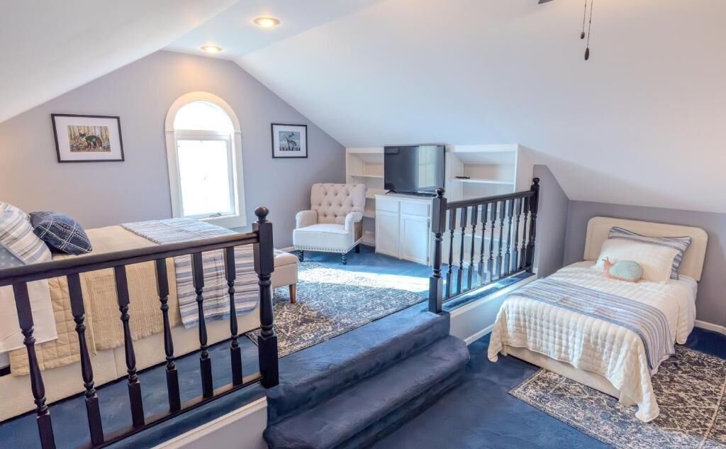 A bedroom with a bed, a chair, a television, and a staircase.