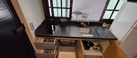 Cocina compacta con encimera negra, un lavabo, un refrigerador pequeño y cajones de almacenamiento abiertos.