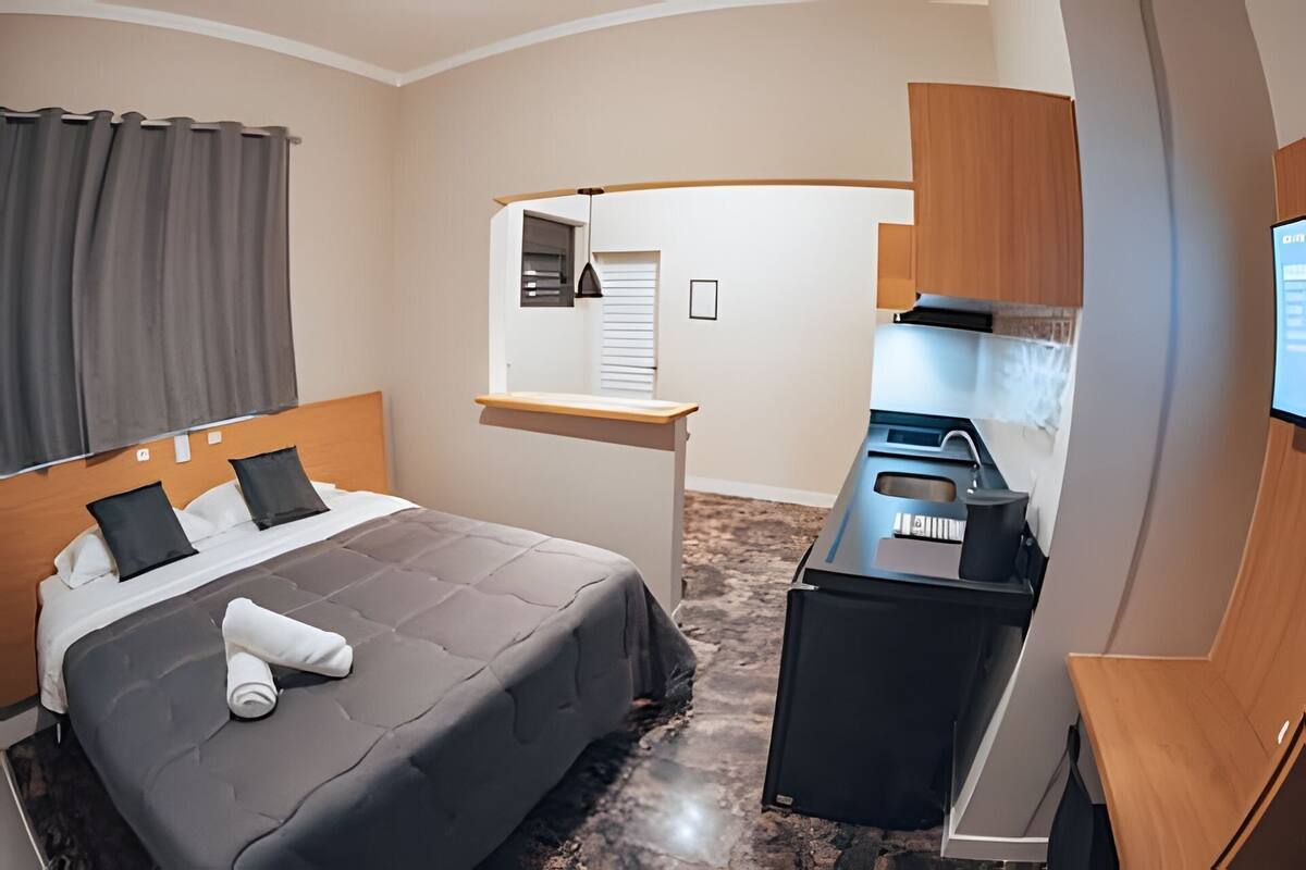 A hotel room with a bed, a small kitchenette, a desk, and a mirror.