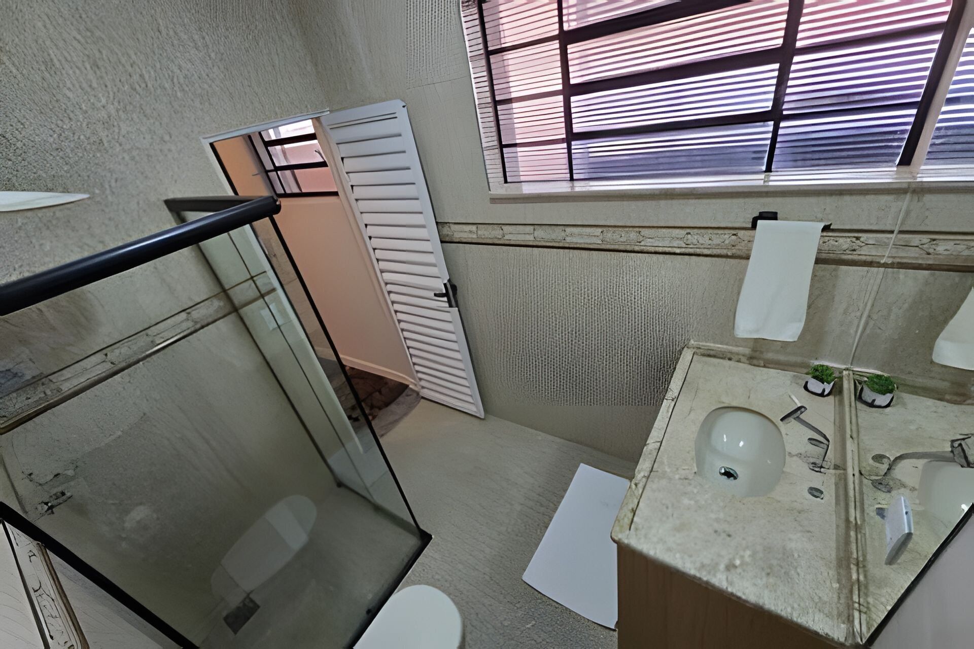 Une salle de bain avec des toilettes, un lavabo et une fenêtre avec des stores.