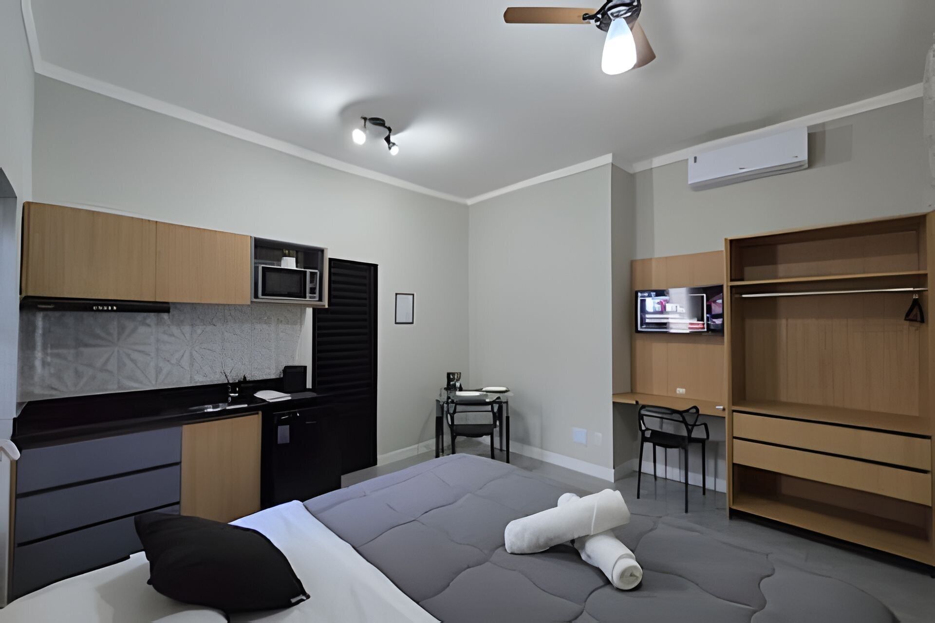 Ein kleines Zimmer mit Bett, einer Küchenzeile, einem Fernseher und einem Kleiderschrank.