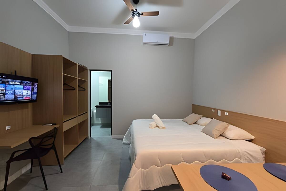 A hotel room with a bed, a desk with a chair, a television, and a ceiling fan.