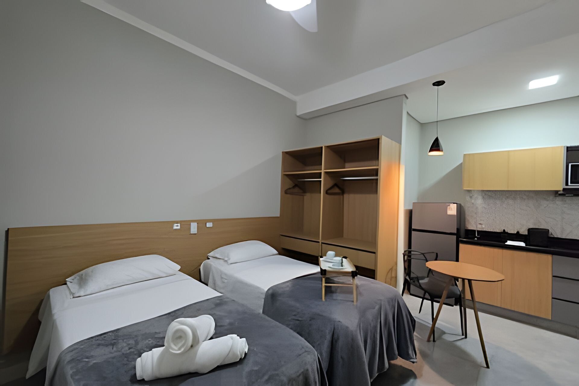 A hotel room with two beds, a small table, a chair, a kitchenette, and a closet.
