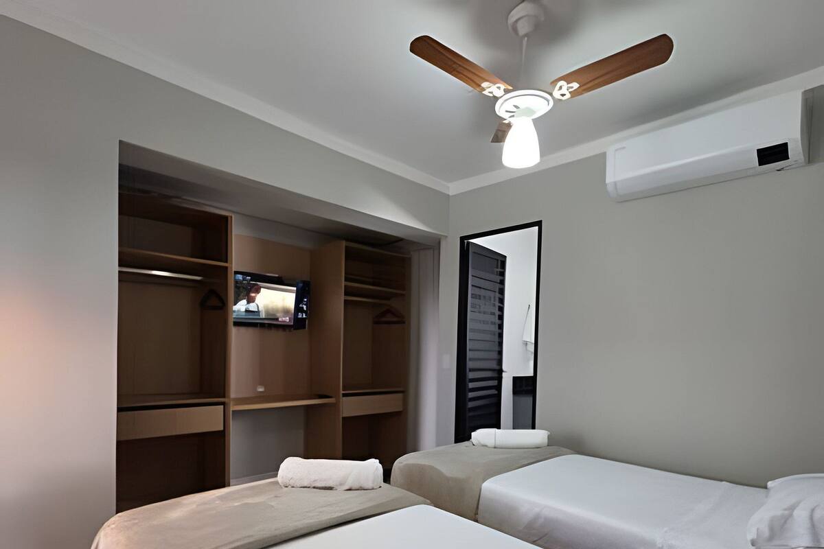 A hotel room with two beds, a ceiling fan, a TV mounted on a wardrobe, and a large mirror.