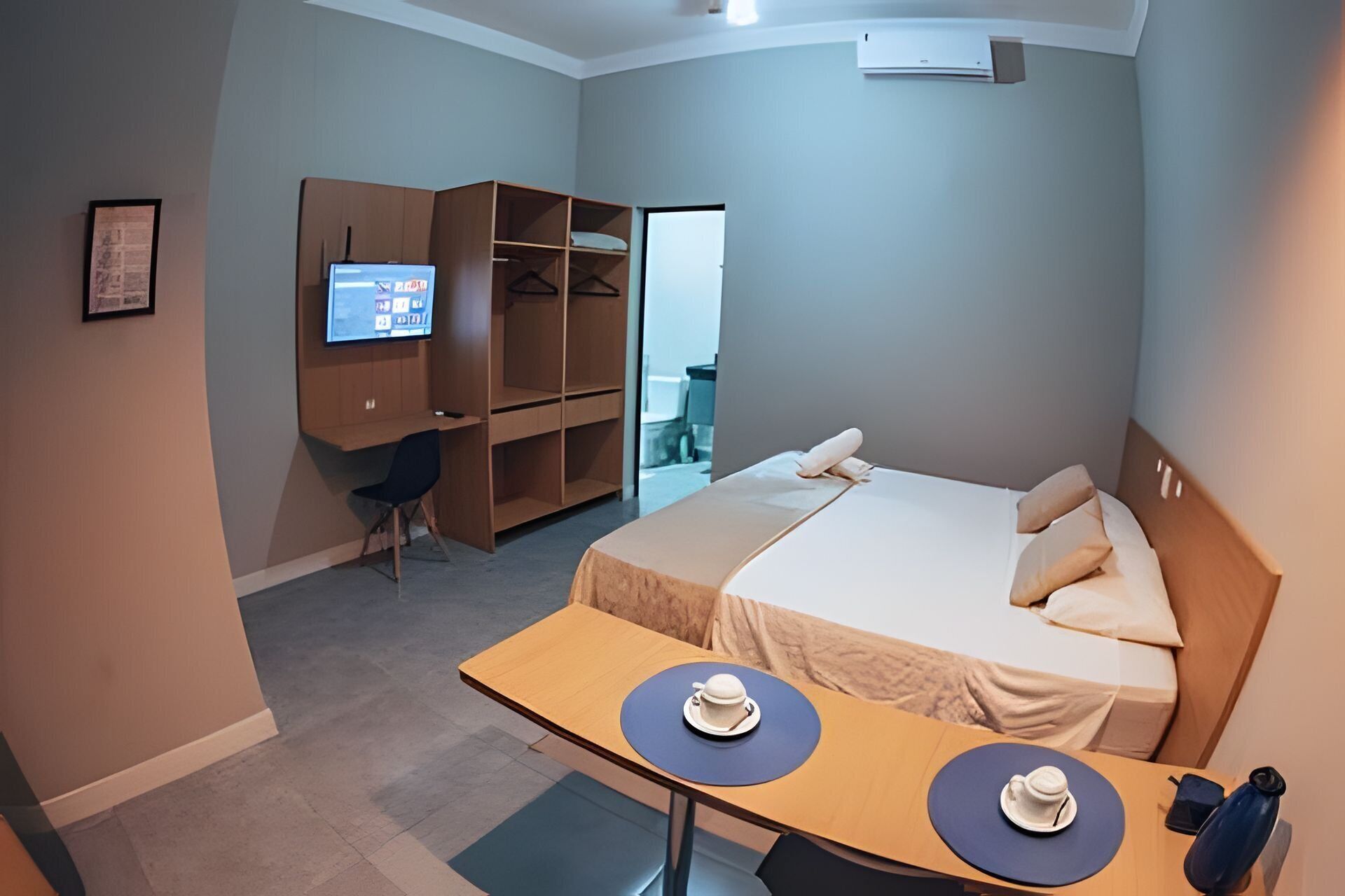 Una habitación de hotel con cama, escritorio con dos tazas, televisión y armario.